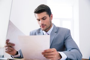 Confident businessman sitting at the table in office and reading documents